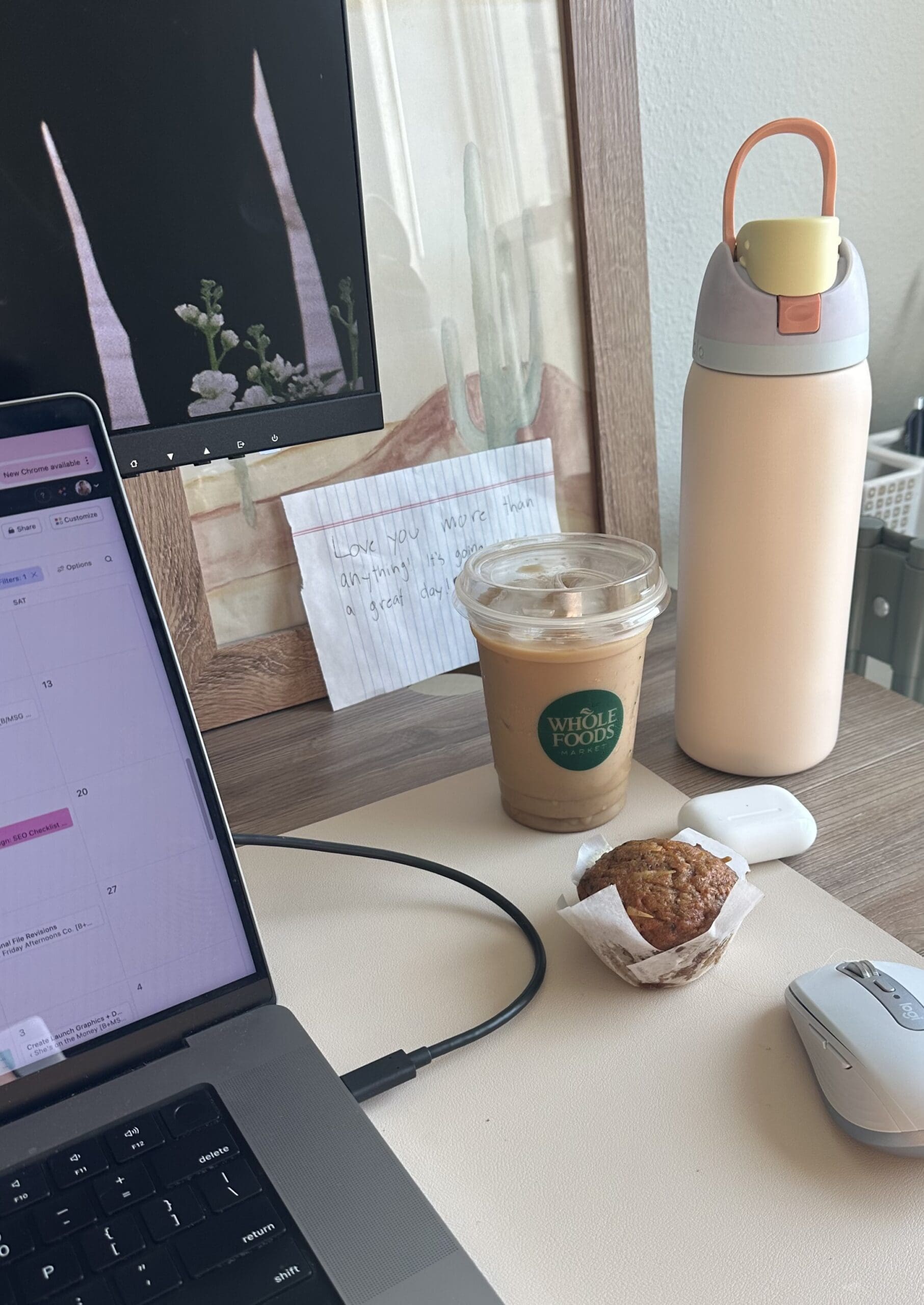 A photo of a messy desk with a laptop, iced coffee, and muffin